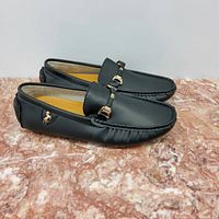 Photo of a pair of men's black leather loafers with gold buckle details, size 41, placed on a marble surface.