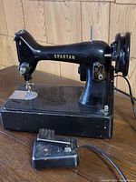 Side view of the black Singer Spartan sewing machine on its base with attached foot pedal in front.