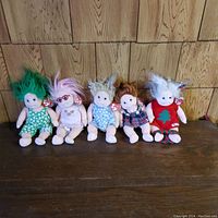 Photo of five Ty Beanie Babies plush dolls lined up, displaying different hair colors and outfits, each with Ty tags visible.