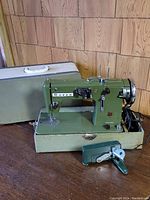 Full view of the green Vigorelli Queen sewing machine on base, with attached foot pedal and power cord, hand crank next to it, and vintage light green hard carrying case behind.