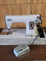 Full view of the off-white vintage Brother sewing machine on a metal base with foot pedal on wood background.