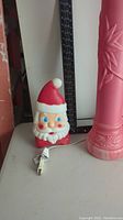 Photo showing Santa Claus head blow mold light, next to a pink torch light with power cord and a ruler for size reference.