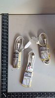 Image showing three individually wrapped white small extension cords with attached specification tags placed beside measuring tape for size reference.