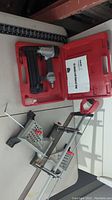Photo showing 18 gauge air nailer in red carrying case and Craftsman miter saw placed on a white surface.