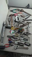 Various hand tools laid out on a table showing assortment including pliers, wrenches, hammer, tape measure, and screwdrivers.