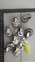 Ten casters arranged flat, showing metal body, wheels, and threaded mounting stems; includes locking casters and plastic clips