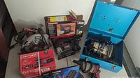 Photo showing the Skil circular saw, Craftsman boxed palm sander and scroll saw, Panasonic battery charger, Craftsman router in blue metal case, and drywall screw driver without cord.