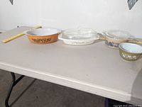 Five vintage Pyrex glass bakeware pieces lined up on a table, showing various floral patterns and colors.