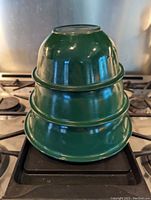 Nested set of three green Pyrex mixing bowls stacked inside each other showing their glossy green finish and size variation.