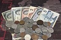 Canadian banknotes and coins spread over a dark map surface showing variety of denominations.