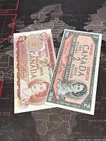 Two Canadian 2 dollar banknotes from 1954 and 1974 laid flat, showing front sides with portraits of Queen Elizabeth II.