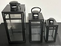 Full view of all three black metal and glass lantern candle holders in large, medium, and small sizes.