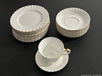 Full set including stacked dinner plates, saucers, and a teacup on saucer showing the shape and gold accents