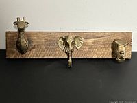 Full view of wooden board with three cast iron animal head hooks: giraffe, elephant, and bull.