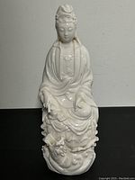 Front view of white Chinese porcelain figurine showing seated person in robes with dragon design on base.