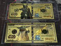 Fronts of two gold foil $100 Star Wars banknotes: top depicting The Mandalorian, bottom depicting Grogu