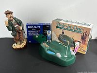 Lot arranged with the figurine, box of electric ball retriever, and Hole-in-One putting game showing the green and two small golfer figurines next to original box.