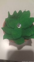 Close-up overhead view of green felt succulent leaves with rhinestone embellishment inside terracotta pot.