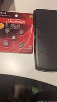 Scientific calculator with its black cover open placed next to a pack of new Sunbeam button cell batteries AG13/LR44.