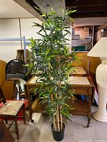Full height view of the vintage faux bamboo plant showing multiple leafy stalks from the black pot. Surrounded by furniture and a white floor lamp.