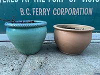 Blue ceramic plant pot with braided rim and tan ceramic plant pot side by side, placed on concrete ground