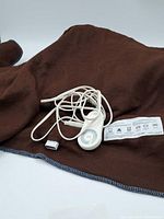 Brown textured mattress pad with blue stitched edge visible, attached white remote control with dial and power cords neatly laid out