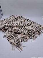 Photo of beige and brown plaid patterned scarf with fringed ends laid flat showing the full cloth texture and pattern.