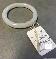 Photo showing white jade bangle bracelet laying flat with a string-tied tag indicating it is a bracelet with 2.5" size.