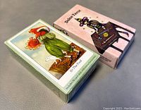 Photo showing the box of The Dreaming Way Tarot and Delos Tarot card deck sides by side on a grey surface.