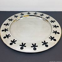 Front view of round Alessi stainless steel serving tray with stylized black human figure cut-outs around the rim.