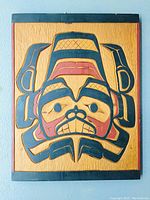 Full view of hand-carved cedar panel showing beaver design painted in black and red on natural wood background.