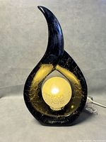 Front angled view of black marble-effect teardrop lamp with lit frosted globe showing internal light