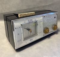 Side angled view showing the black casing, clear front panel with clock, tuning knobs, and gold control buttons on top.
