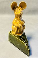 Full view of the mouse sitting on the green cheese wedge coin bank showing the right side with coin slot and cheese bite detail.