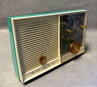 Angled front view of Philco model 722 vintage desktop radio and clock with turquoise casing, showing speaker grille, tuning knob and clock face with gold-tone hands and dials.