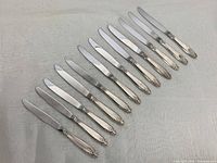 Full set of twelve dinner knives with sterling silver handles showing floral embossed design.