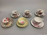 All six teacup and saucer sets arranged in a group showing various floral designs and month labels on some cups.