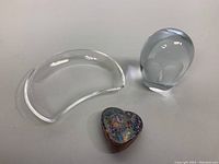Photo showing all three items together on a flat surface: clear half-moon Lalique plate, clear crystal owl paperweight, and colorful heart paperweight with speckled glass