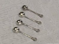 Four sterling silver miniature spoons laid out to show size, shape, and handle design.