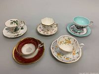 Overview of all five assorted bone china teacup and saucer sets showing varying colors and patterns.