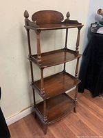 Full view of antique wooden etagere bookcase showing four shelves, turned wood pillars, decorative finials, and shaped back panel on top shelf.