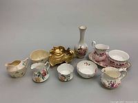 Full display of the various china and porcelain items including vases, bowls, and creamers with floral and gold leaf patterns.