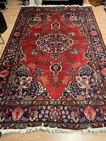 Full view of handmade Turkish wool carpet on wooden floor showing red field with intricate floral and medallion pattern, bordered with floral designs and fringed edges.