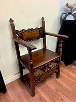 Three-quarter view showing overall chair form, armrests, carved backrest and front stretcher