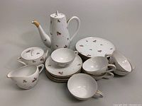 Full view of tea set including coffee pot, sugar bowl, creamer, stacked plates, and teacups with saucers