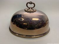 Front side view of the large silver plated meat dome, showing its rounded shape, smooth finish and reflective surface.