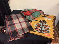 Three wool blankets laid on a black surface, including a plaid and a patterned colorful tapestry.