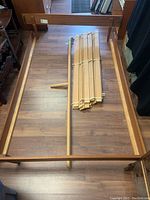 Full view of teak twin bed frame laid out on wood floor with bundled wooden slats and center support rail visible.