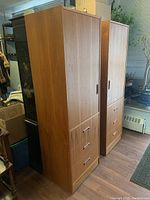 Two identical teak veneer cabinets side by side on casters in showroom