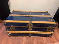 Front view of the large blue steamer trunk with wood slats, shows the metal latch and corner brackets, wood slats horizontally and vertically across trunk surface.